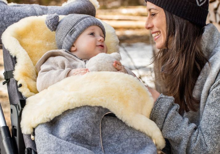 Baby in Lammfell-Fußsack lächelt Mutter an, die daneben kniet